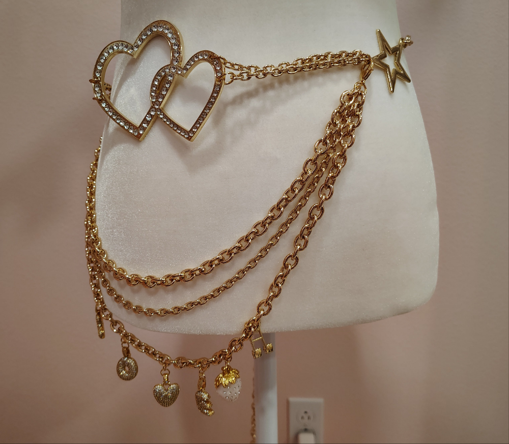 Gold chain belt with heart and star charms on a mannequin against a neutral background