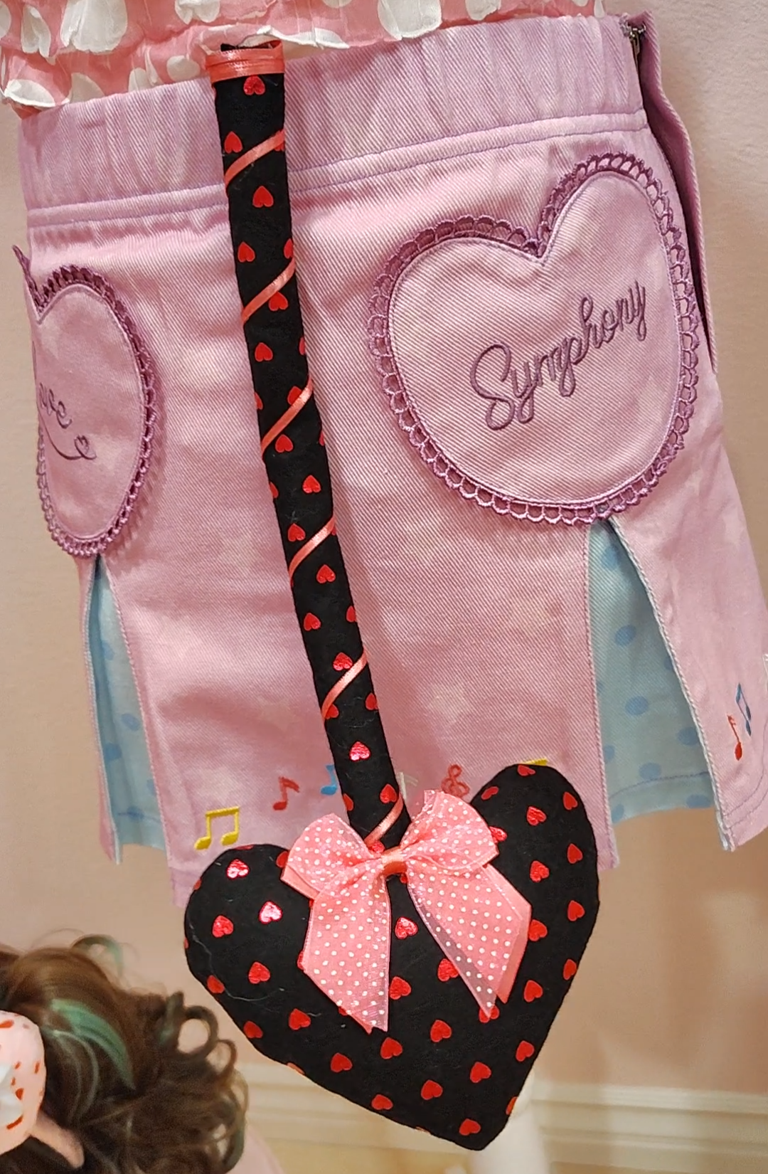 Purple skirt with heart designs and 'Symphony' text, showcasing a black devil tail with heart prong, red herat pattern, and a pink ribbon with pink polkadot bow.