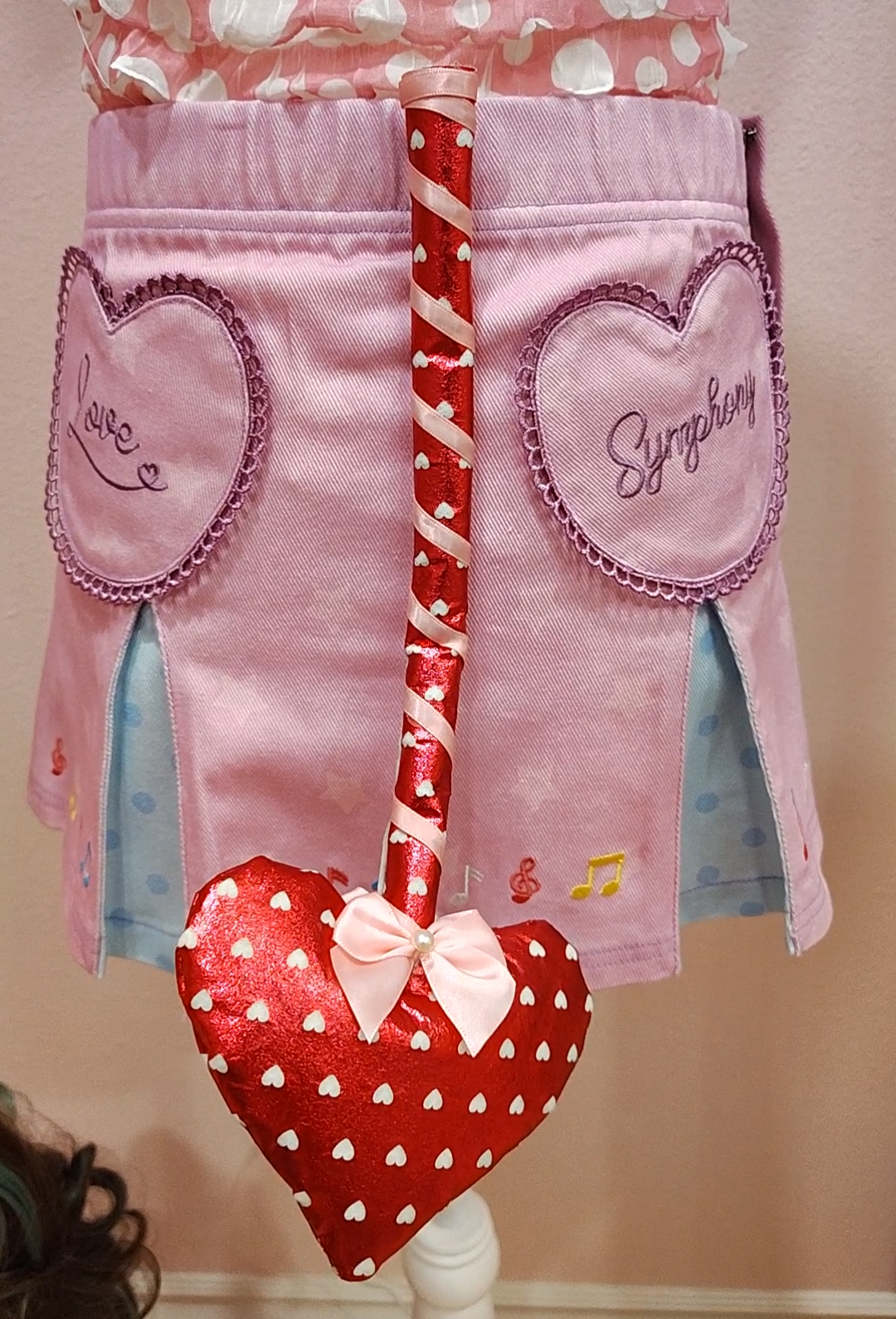 Purple skirt with heart designs and a red devil tail with white heart pattern, heart shaped prong, wrapped in a pink ribbon with a pearl detail.