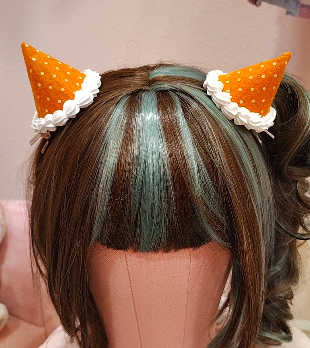 Orange devil horn hair clips with polkadots and white decoden cream on a mannequin head.