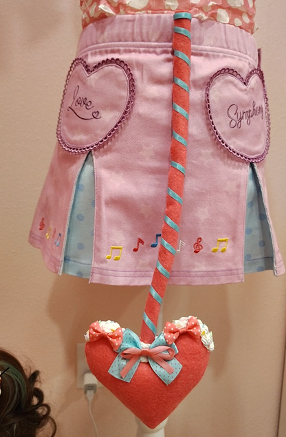 Outfit with purple skirt and pinkish red devil tail accessory with heart tip.