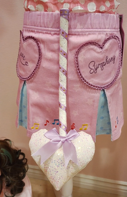 Purple skirt with heart designs and a white sparkly devil tail accessory with a heart prong wrapped in purple ribbon.