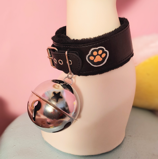 Black leather collar with a paw print design and bell on a mannequin against a pink background