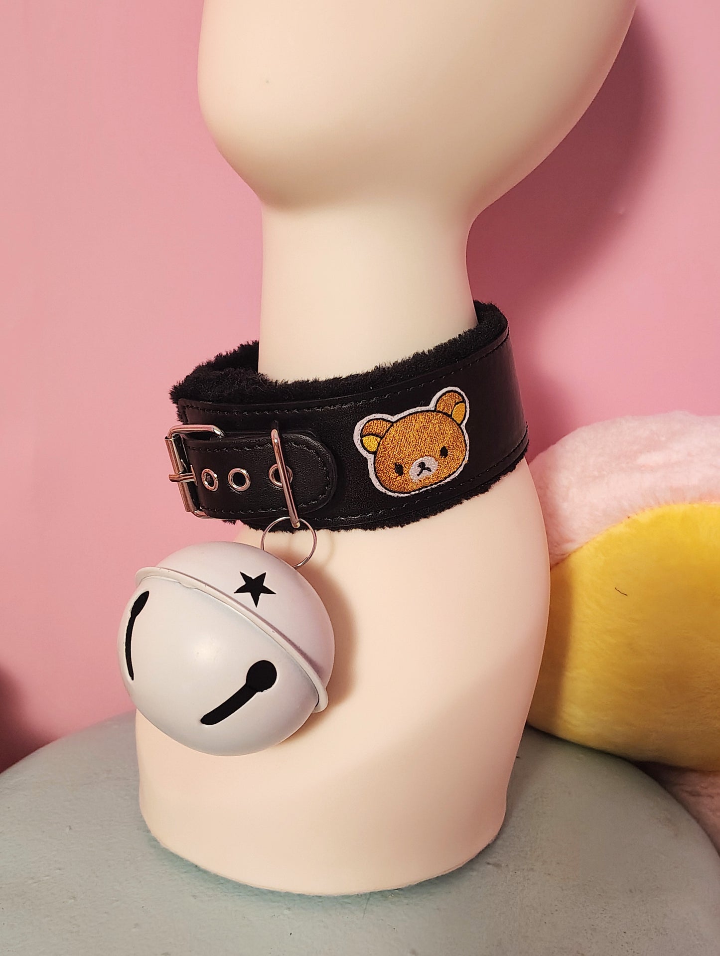 Collar with a bear charm and bell on a mannequin against a pink background