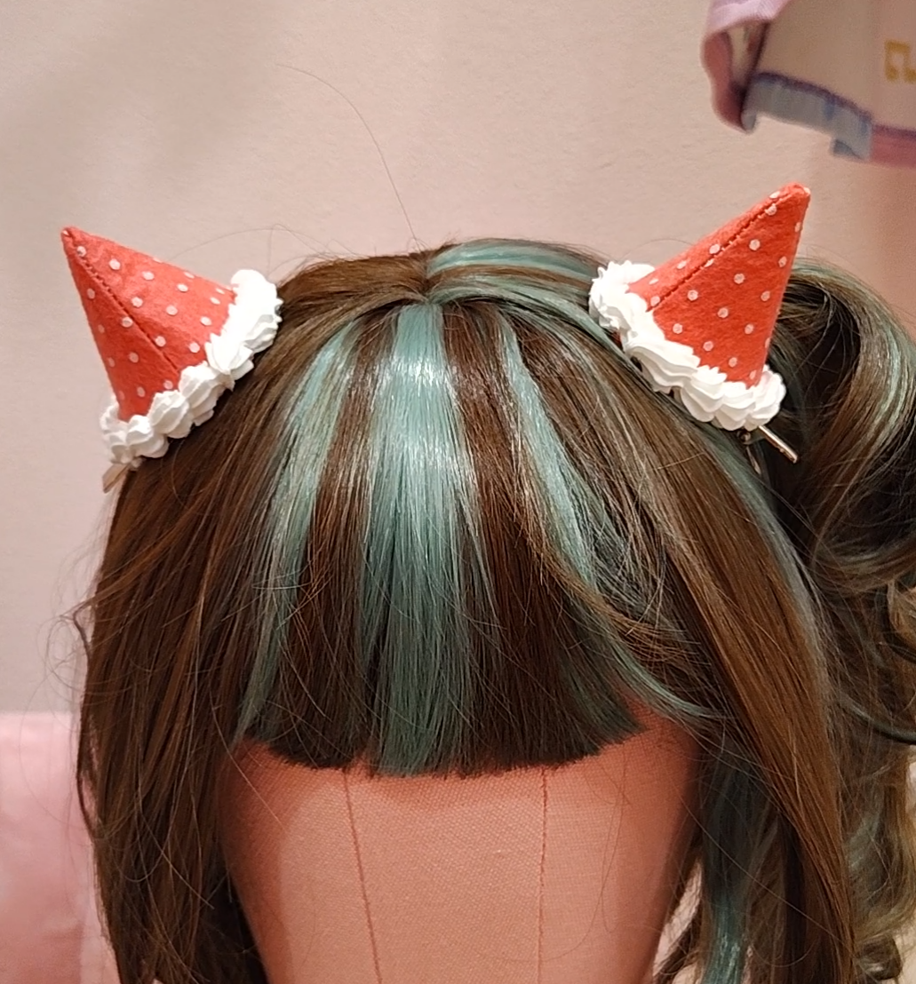 Close up of mannequin head wearing pinkish red devil horn hair clips with white polkadots and decoden cream.