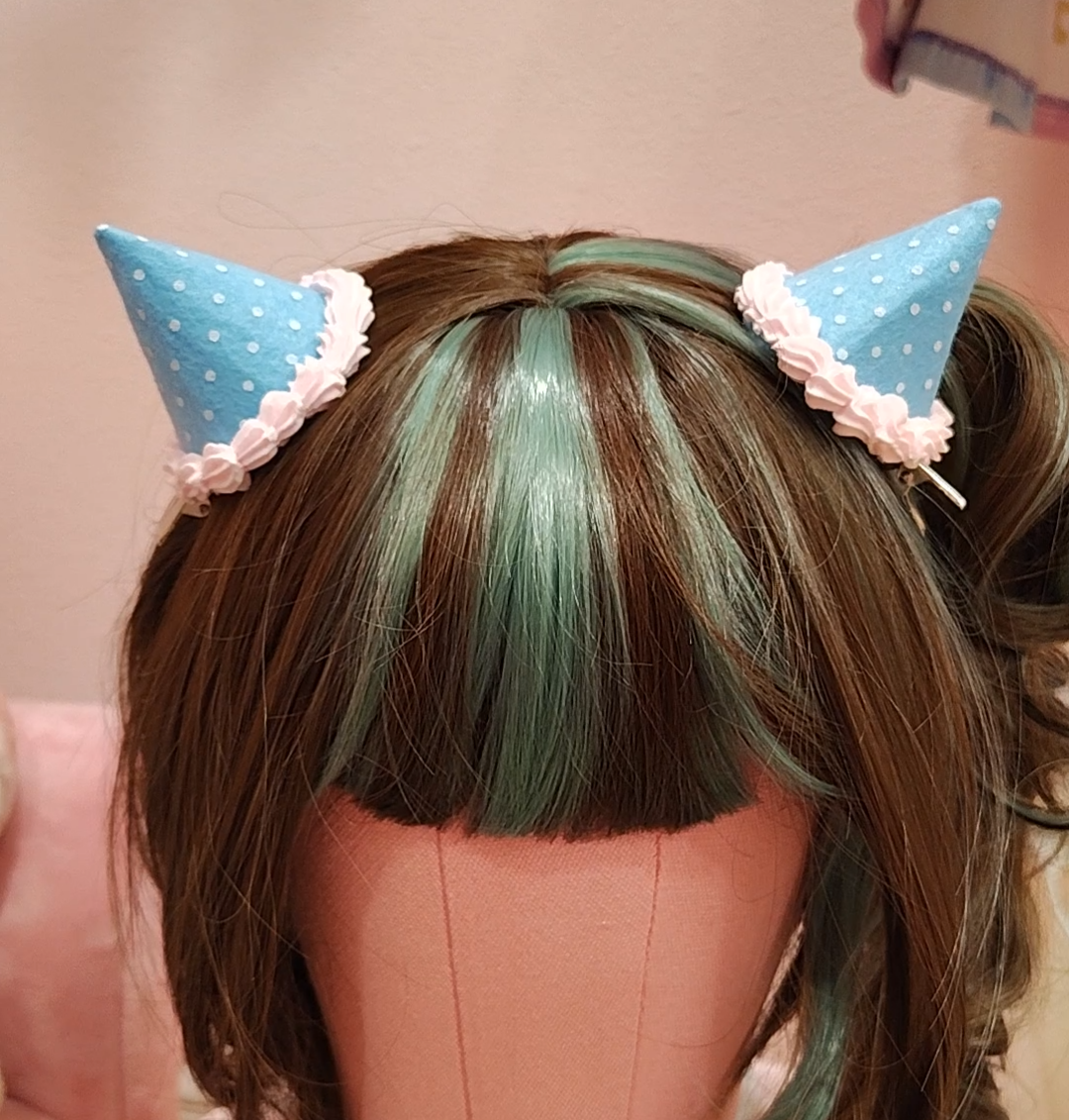 Mannequin head sporting blue devil horn hair clips, with white polkadots and decoden cream.